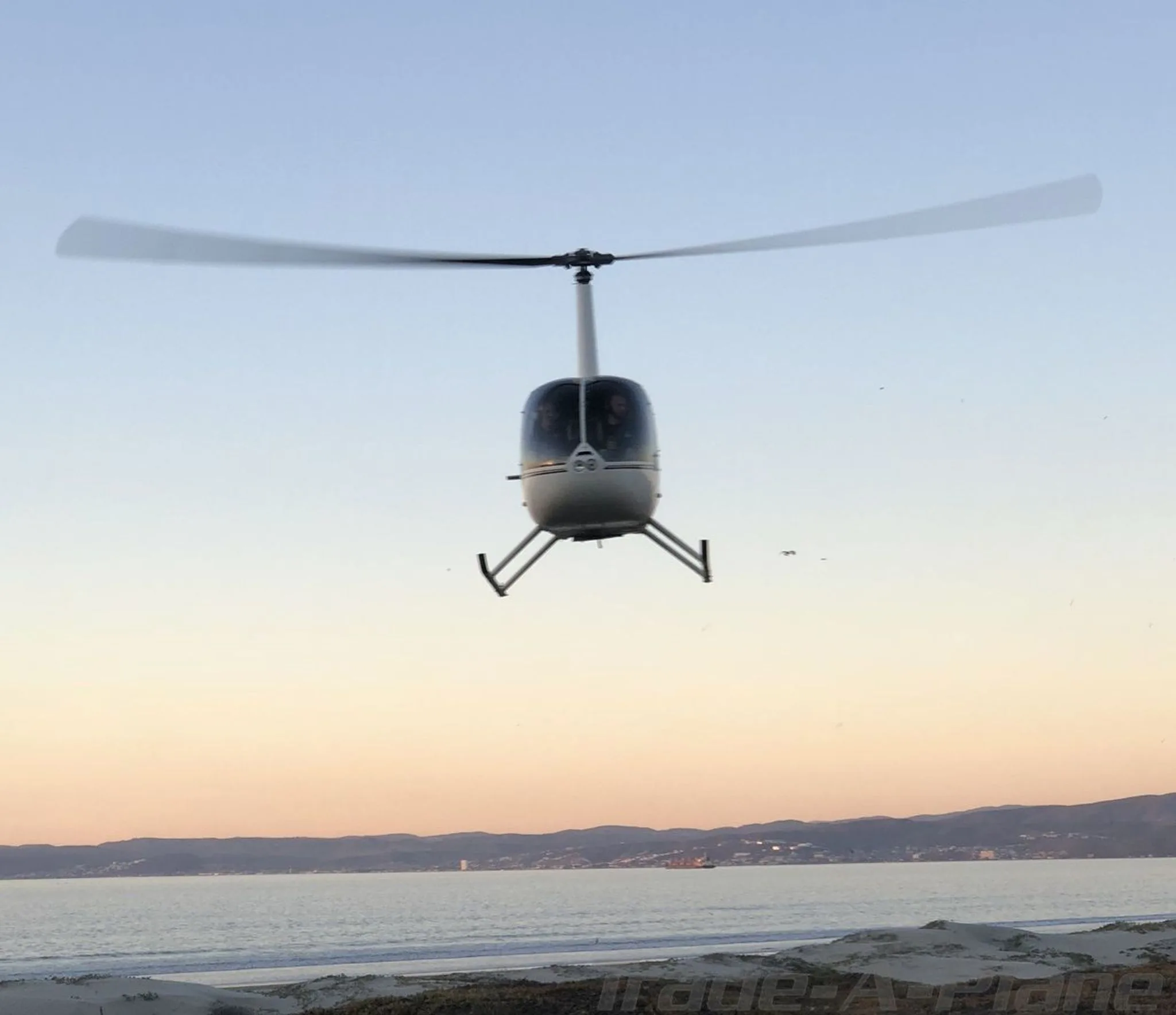 A Robinson R44 Raven I hovering above the beach at dusk.