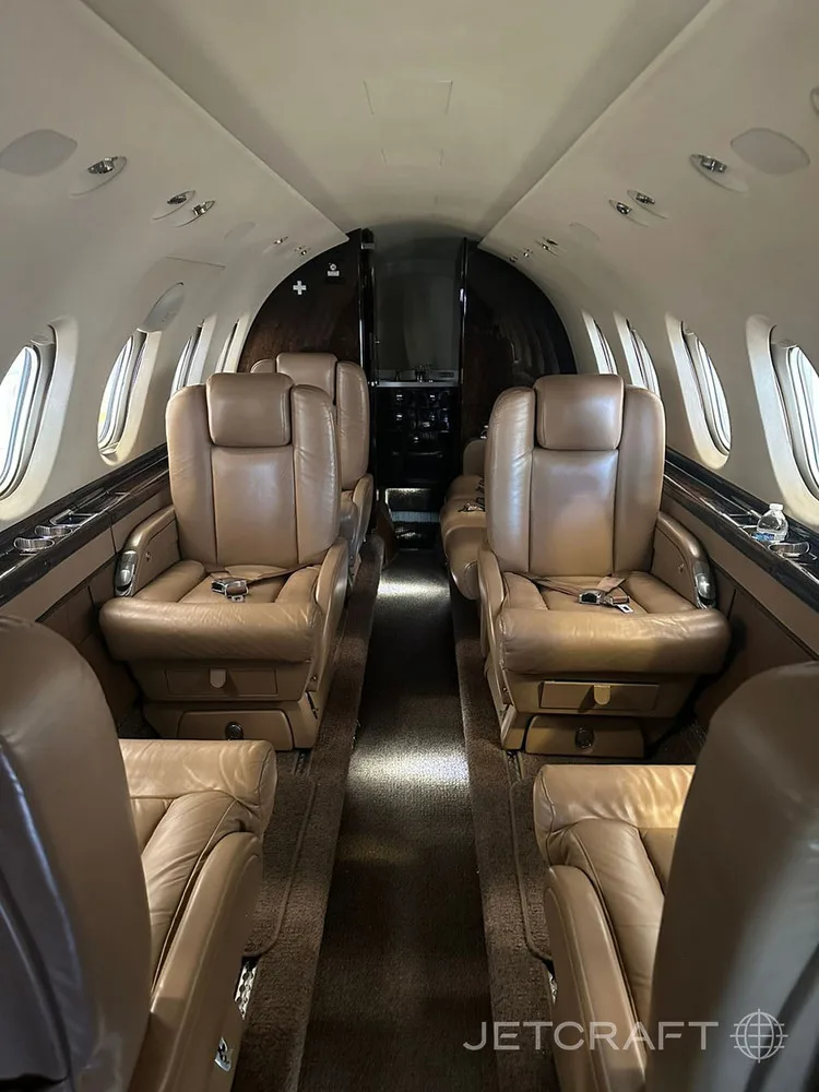 A view down the aisle of a private jet cabin featuring tan leather seats.