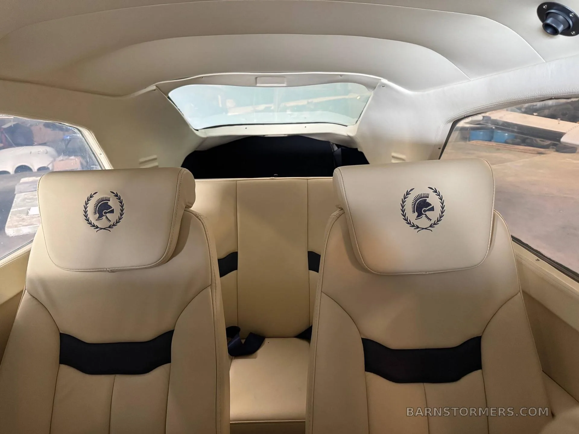 The aircraft's interior features two cream-colored front seats with a dark emblem on the headrests, and a rear bench seat.