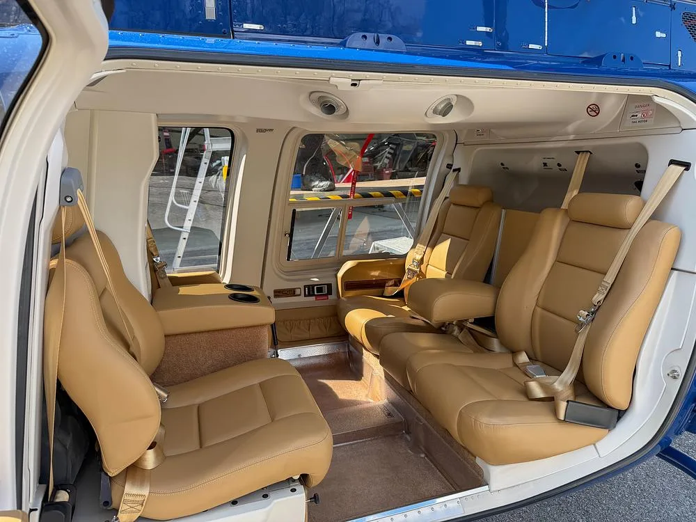 The helicopter's interior features tan leather passenger seats with seatbelts.