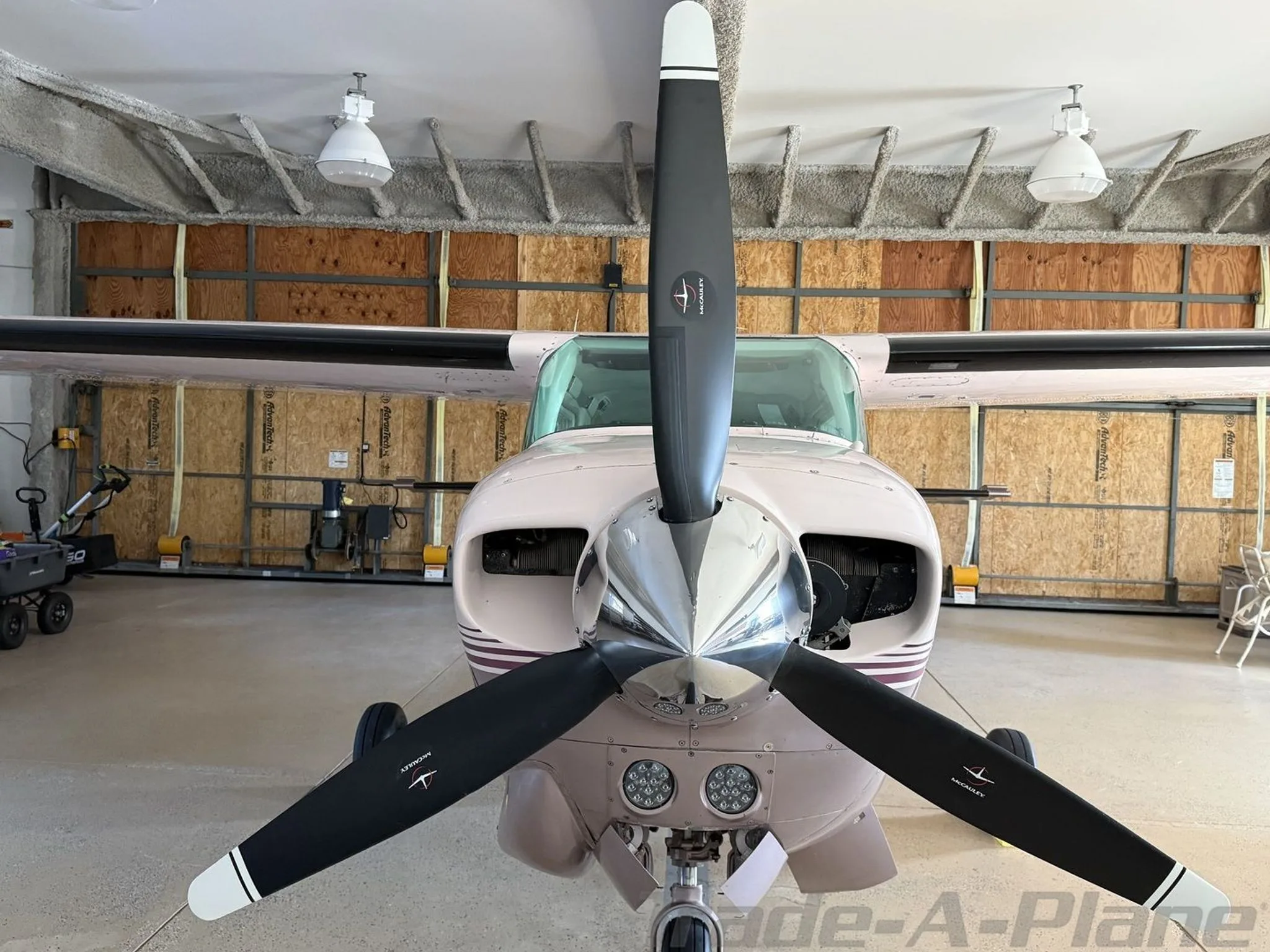 A close-up front view of the propeller and nose of a light pink Cessna 210 Centurion aircraft.