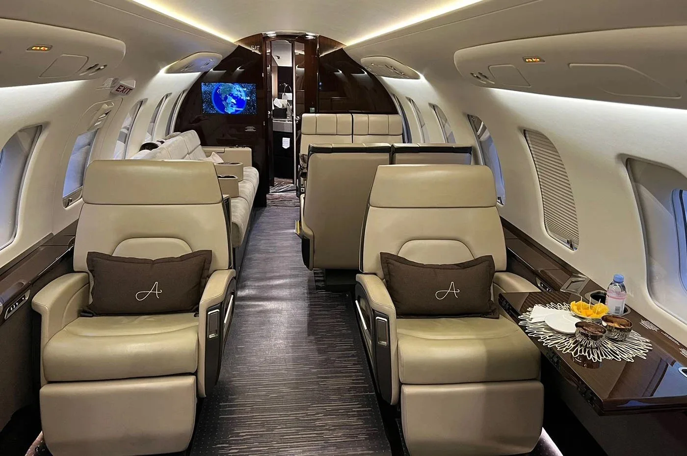 The luxurious interior cabin of a private jet with beige leather seats and dark wood accents.