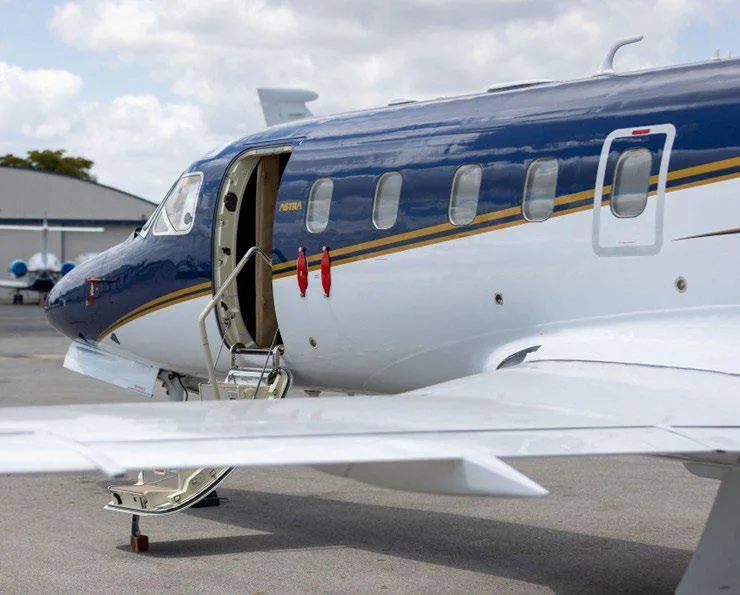 A close-up of the front-left side of a blue and white Astra business jet with its main cabin door open and stairs extended.
