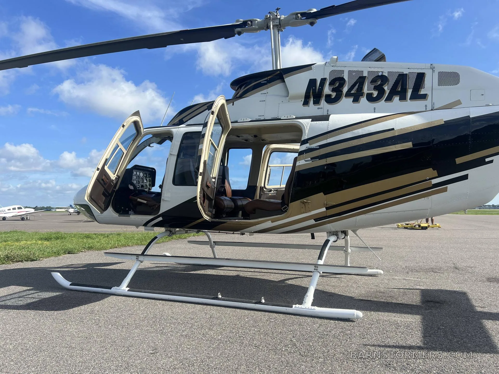 A close-up view of the white and gold Bell 206 helicopter (N343AL) with all its doors open, revealing the brown interior.
