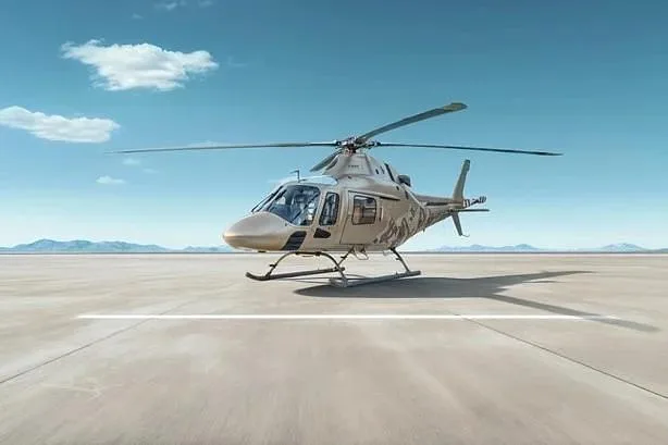 A tan and camouflage-painted helicopter with skids sits on a vast concrete pad under a clear blue sky.