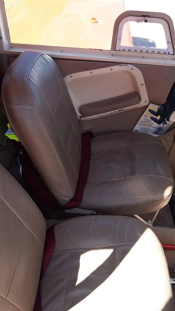 The tan leather front passenger seat and part of the pilot seat in the interior of a Piper Cherokee 180.