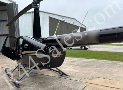 A black Robinson R44 Raven II helicopter with gold pinstripes and an open door is parked on a tarmac, viewed from the side.