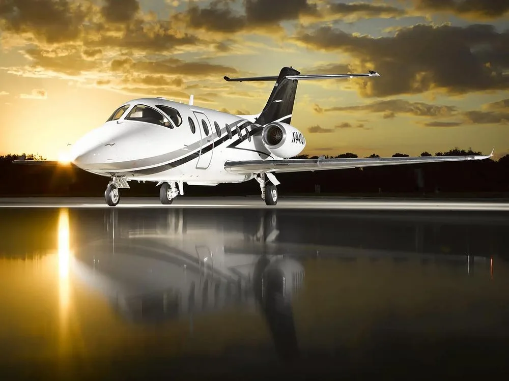 A white Cessna Citation M2 business jet with black and grey stripes, N440LN, parked on a tarmac at sunset.