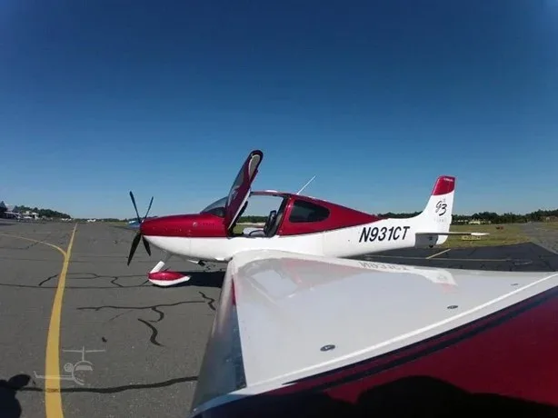 A red and white Cirrus SR22T aircraft, N931CT, with its doors open, parked on an airfield.