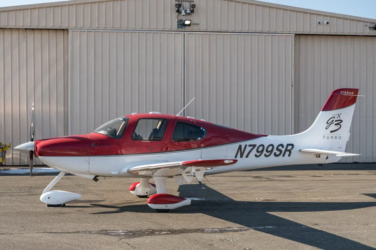 A red and white Cirrus SR22T aircraft, N799SR, parked on an tarmac in front of a hangar.