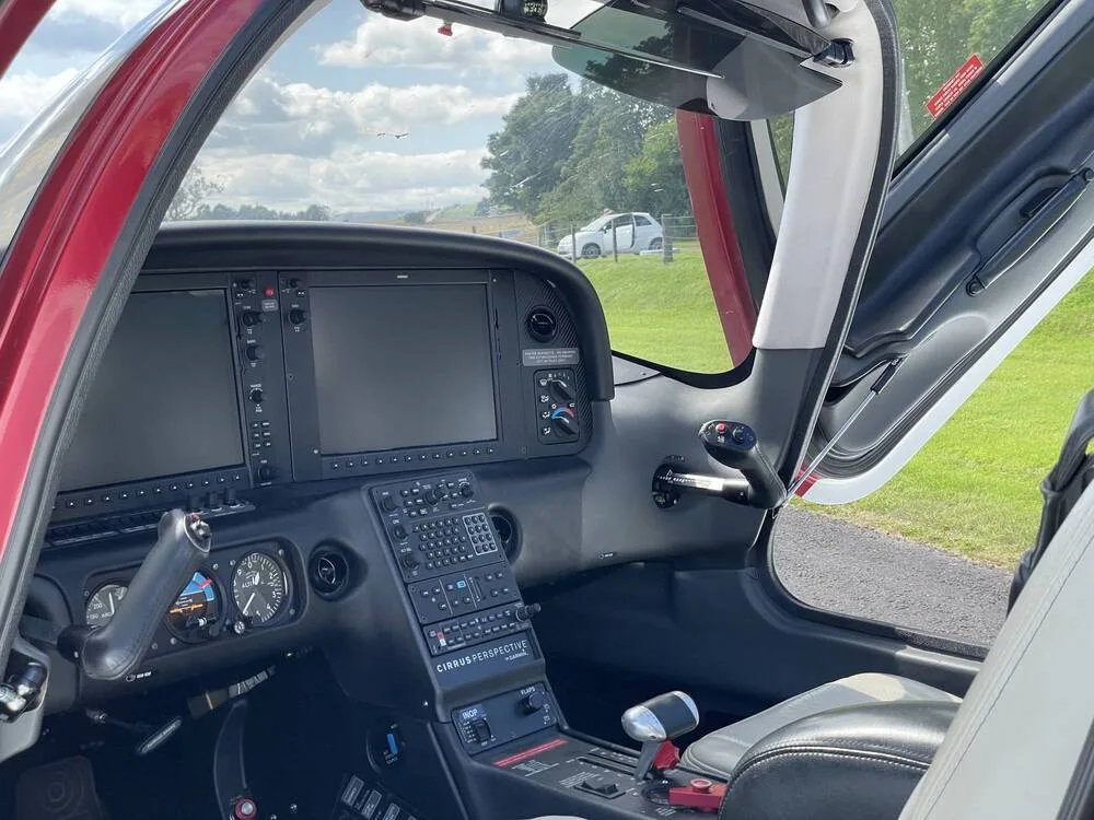 A view of the Cirrus SR22 cockpit showing the instrument panel, controls, and a light-colored seat with the door open.
