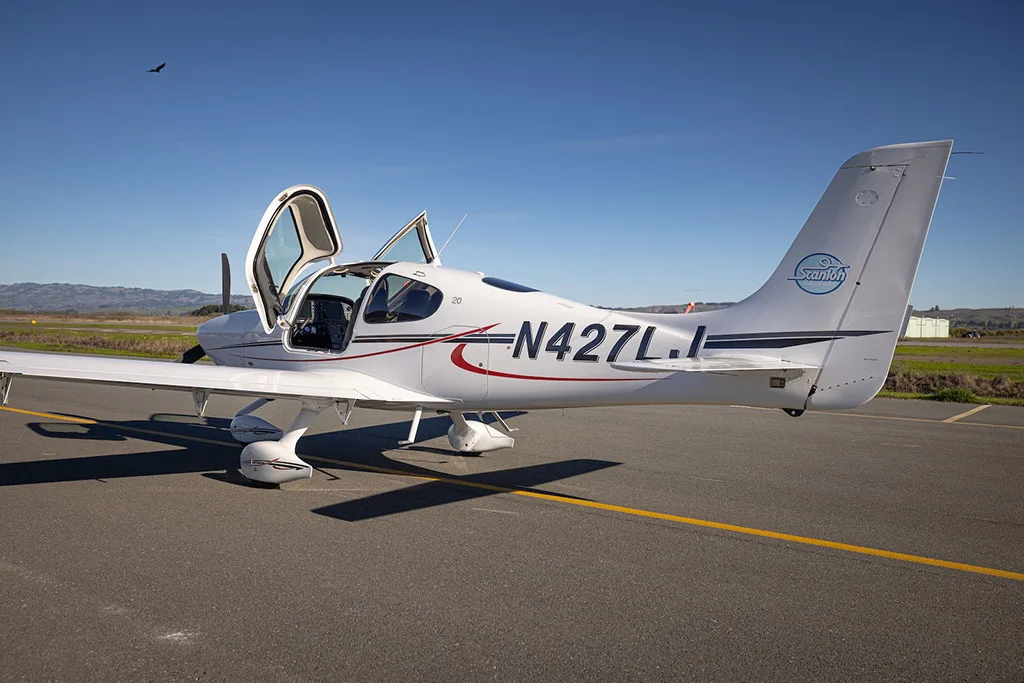A white single-engine aircraft, N427LJ, with its gull-wing doors open, viewed from the rear on an airfield.