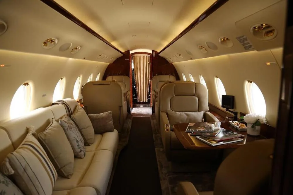 A view of the private jet's cabin showing a comfortable sofa and individual seats with decorative pillows.