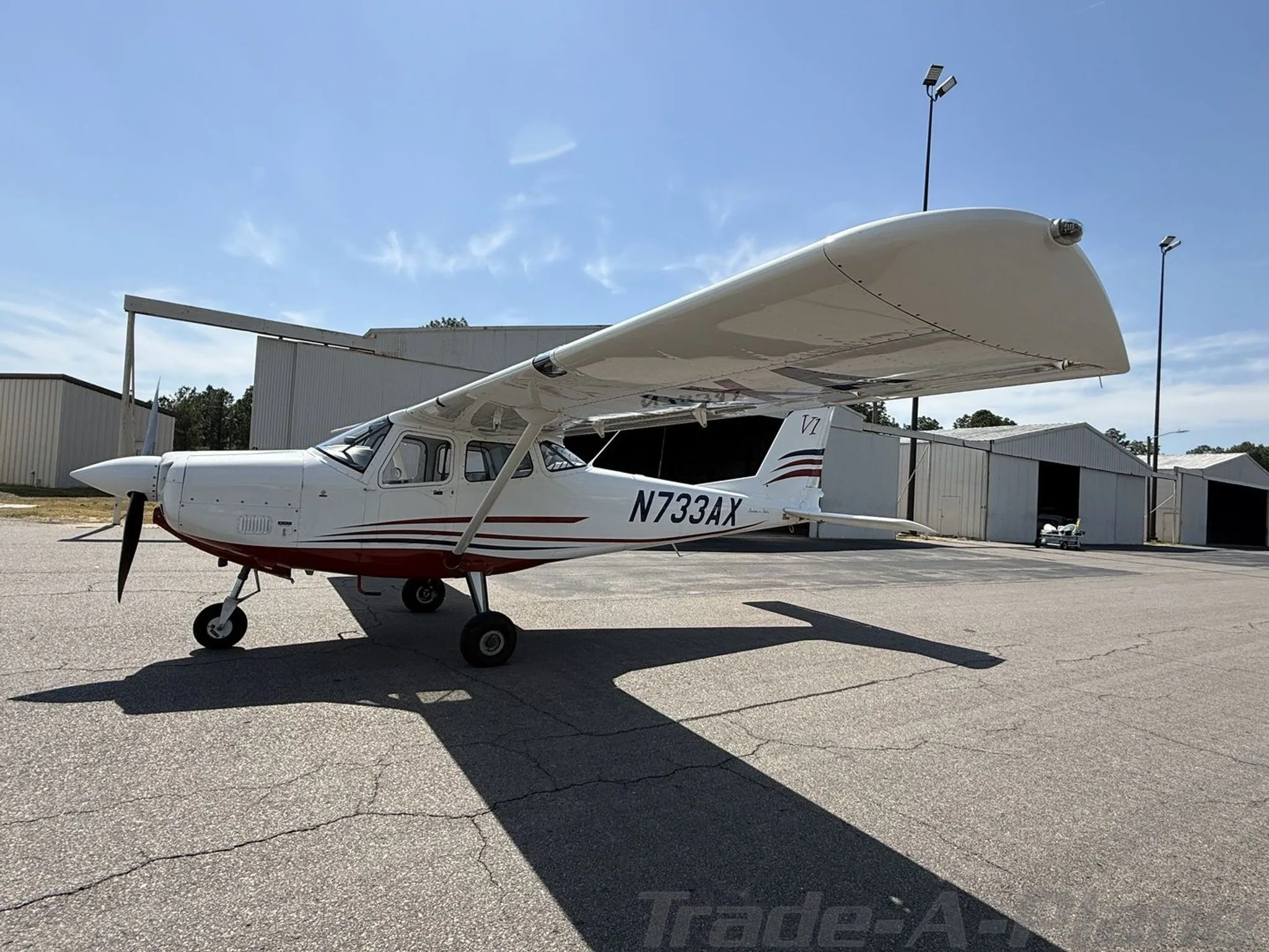 Side view of the white and red single-engine aircraft N733AX parked on an asphalt apron.