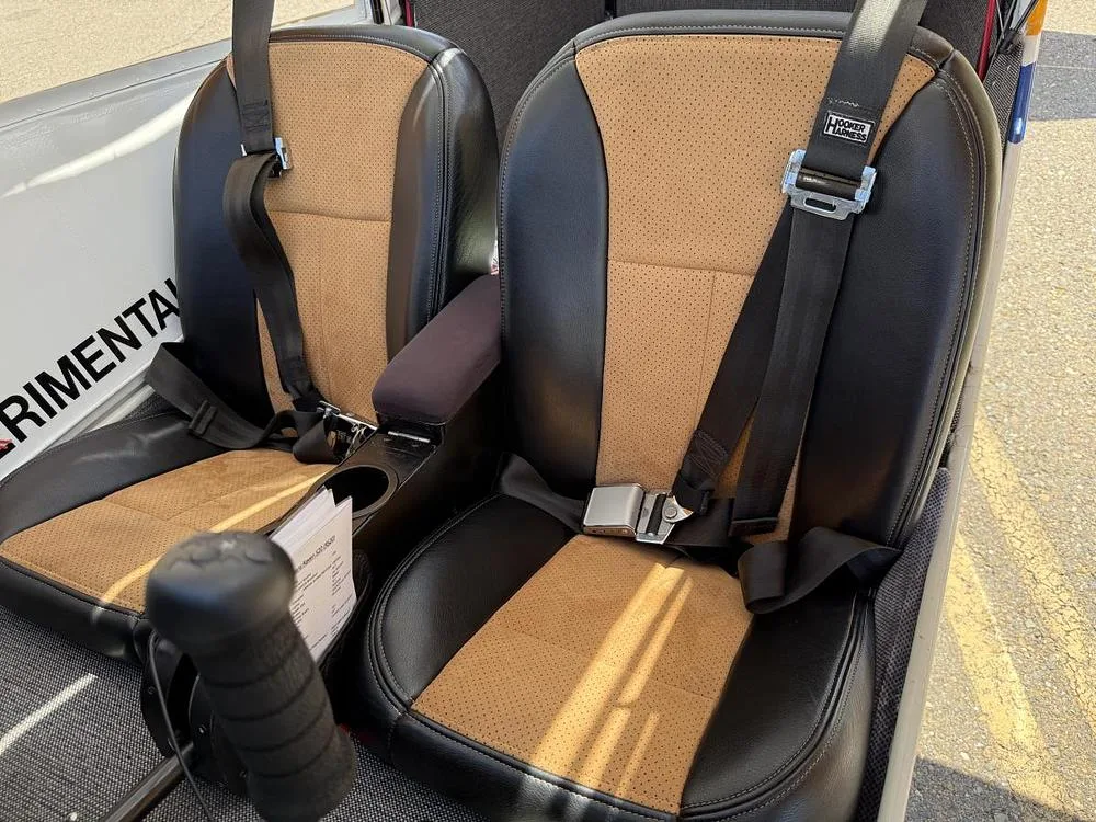 Two tan and black leather aircraft seats with seatbelts are visible in the cabin.