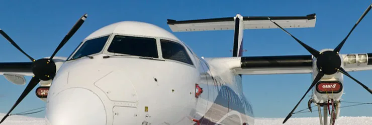 The front view of a white turboprop aircraft, possibly a Dash 8, with propellers visible, parked in a snowy landscape.