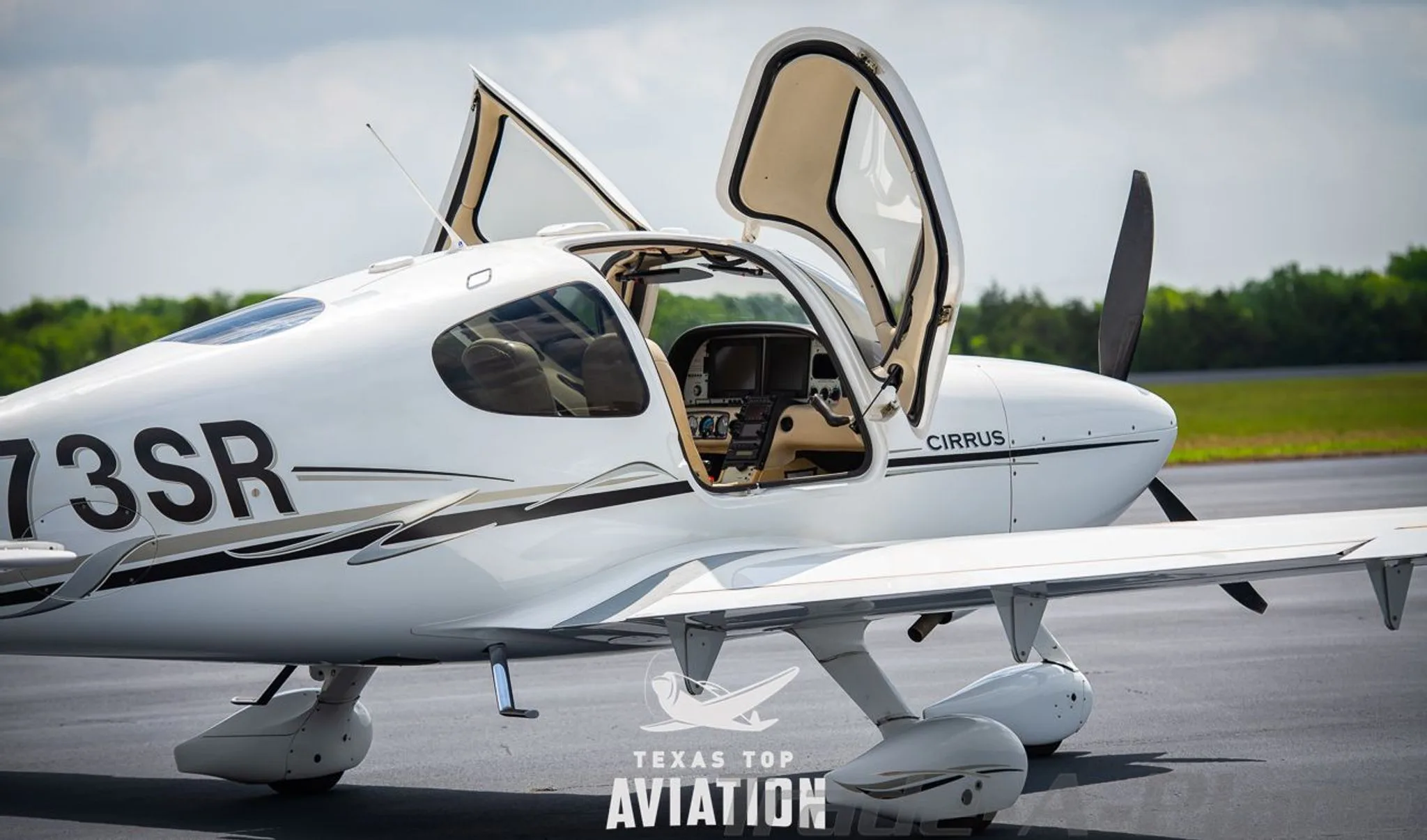 A white Cirrus SR22 aircraft, registration N173SR, parked on an airfield with both gull-wing doors open, showing the interior.
