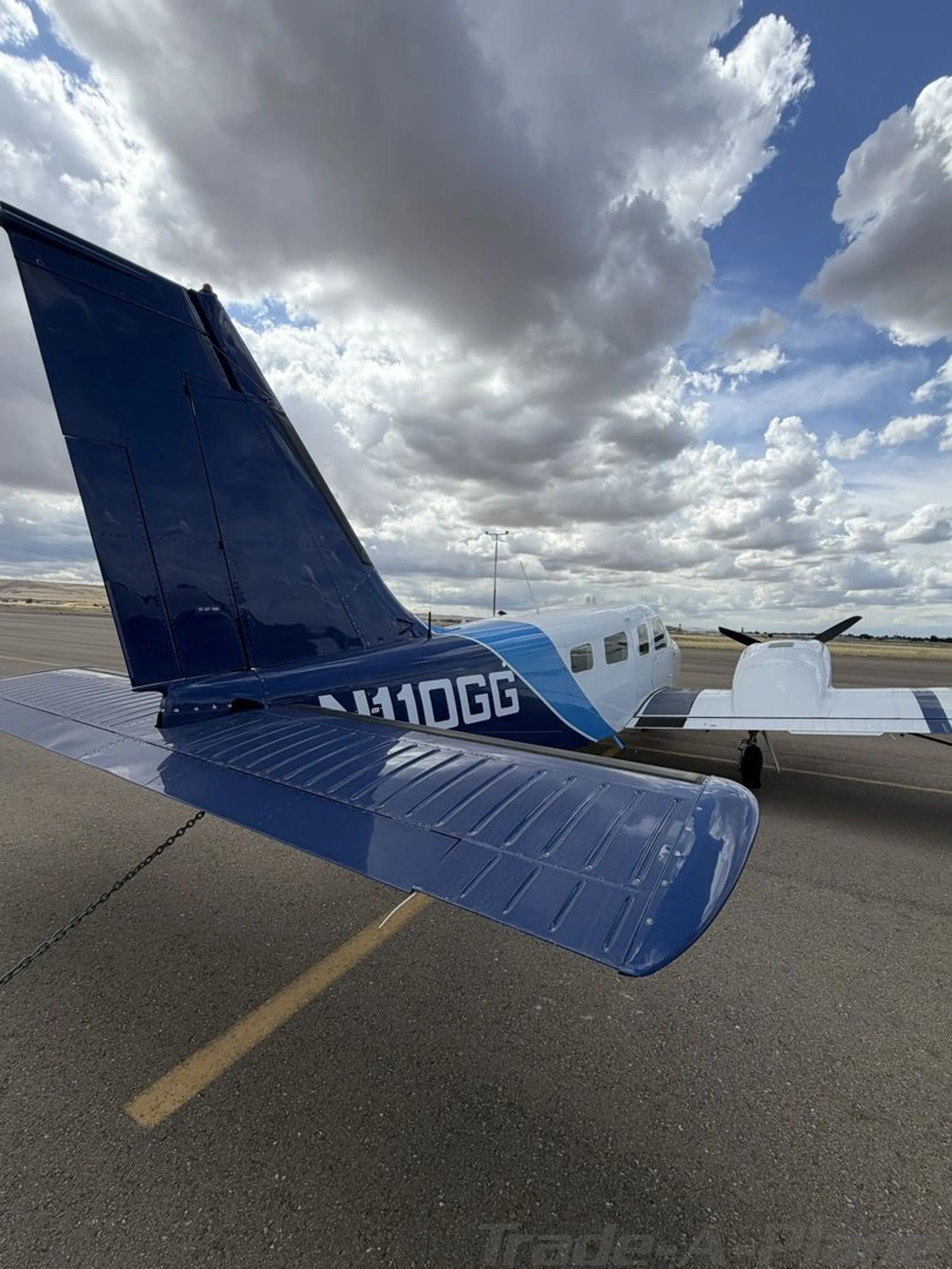 A close-up rear view of the blue tail and horizontal stabilizer of the Piper Seneca II aircraft, showing registration N110GG, on an airport tarmac.