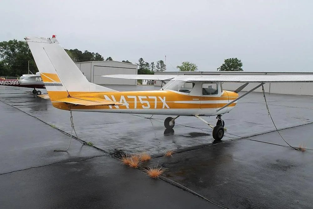 A yellow and white Cessna 150 (or similar high-wing single-engine aircraft) with registration N4757X parked on a wet tarmac.