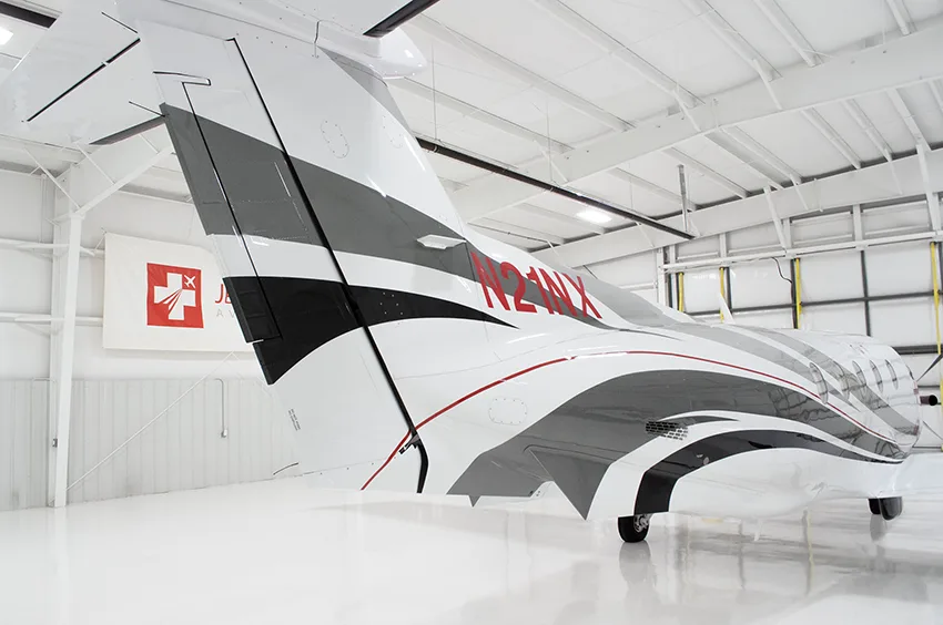 A close-up of the black wingtip with red stripes and the tail of a Pilatus PC-12NG aircraft, showing registration N21NX.