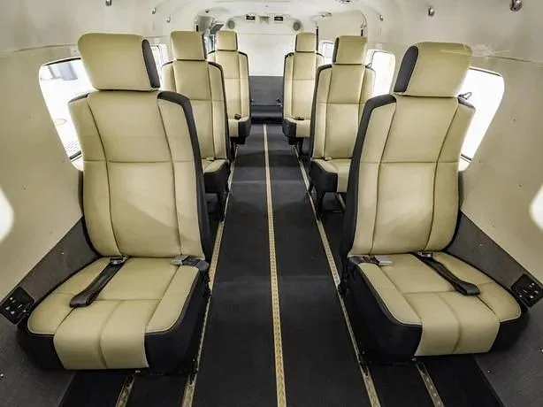 A view down the aisle of an aircraft cabin showing rows of light beige and black passenger seats.