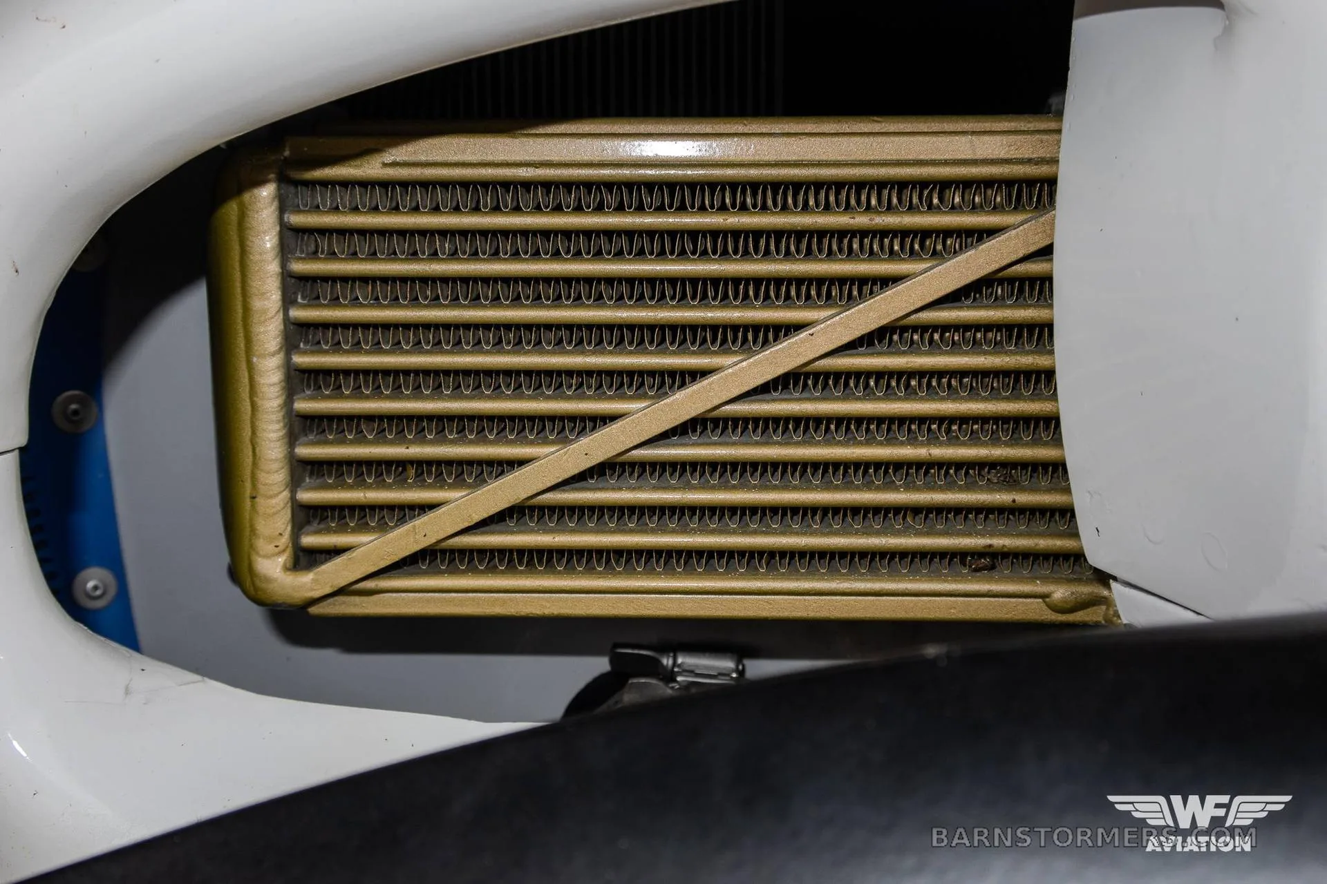 A close-up view of a gold-colored radiator or cooler component inside the white cowling of an aircraft.