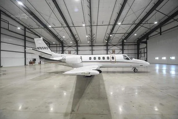 A white business jet with black and gold stripes, tail number N765RD, is parked in a large, empty hangar.