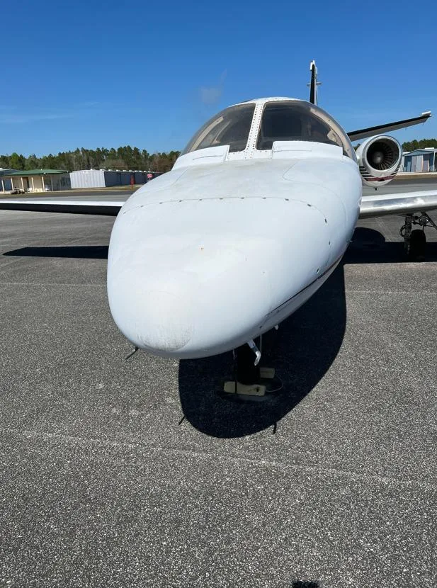 A front view of the white nose of a Cessna Citation I business jet parked on an asphalt tarmac.