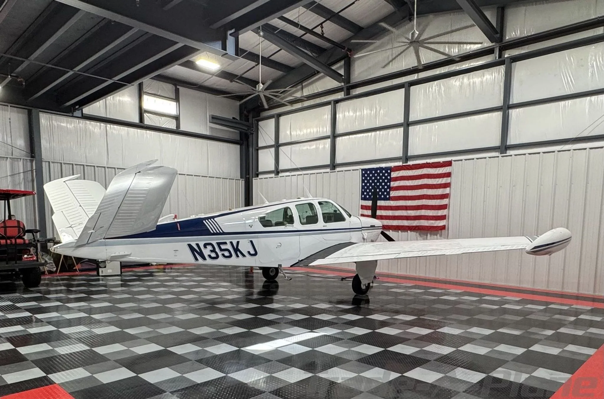 A white Beechcraft Bonanza N35KJ with blue and grey stripes parked in a hangar, showing the V-tail.