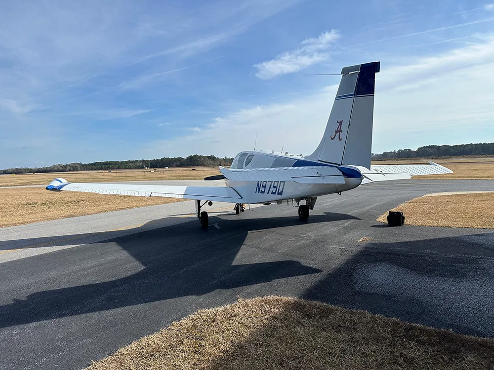 A white and blue Beechcraft Debonair N979Q seen from the rear on a tarmac at an airfield under a clear sky.
