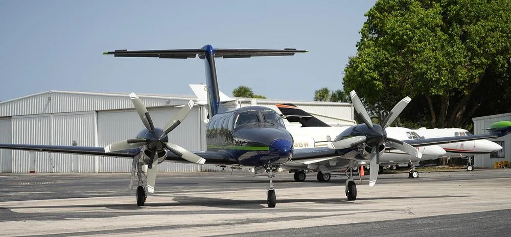 A front view of a dark blue and grey twin-engine turboprop aircraft with a green stripe, parked on an airfield.