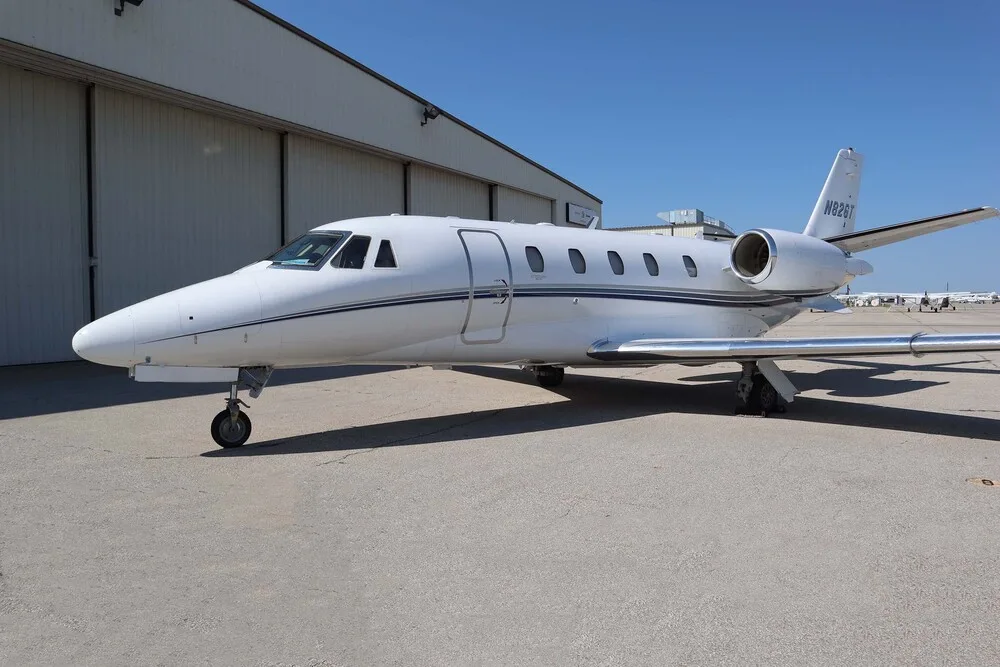 A white Cessna Citation business jet with blue and grey stripes, registration N82GT, parked on a tarmac.