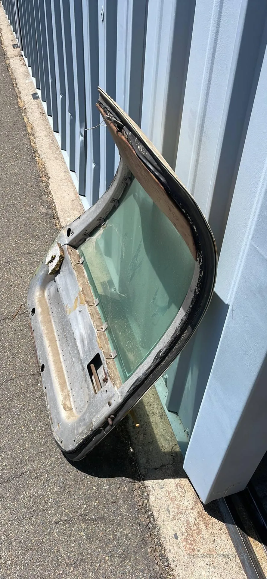 A weathered aircraft door with a window, leaning against a corrugated metal wall.