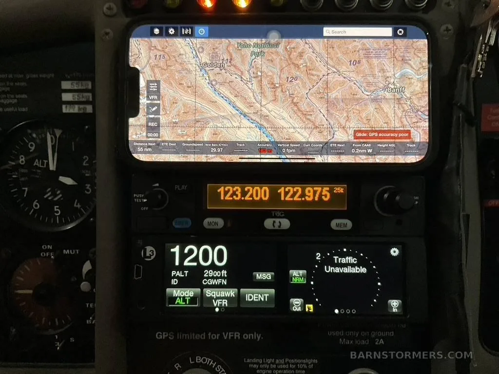 A close-up of the glider's avionics, including a smartphone displaying a map of Yoho National Park and a radio/transponder unit.