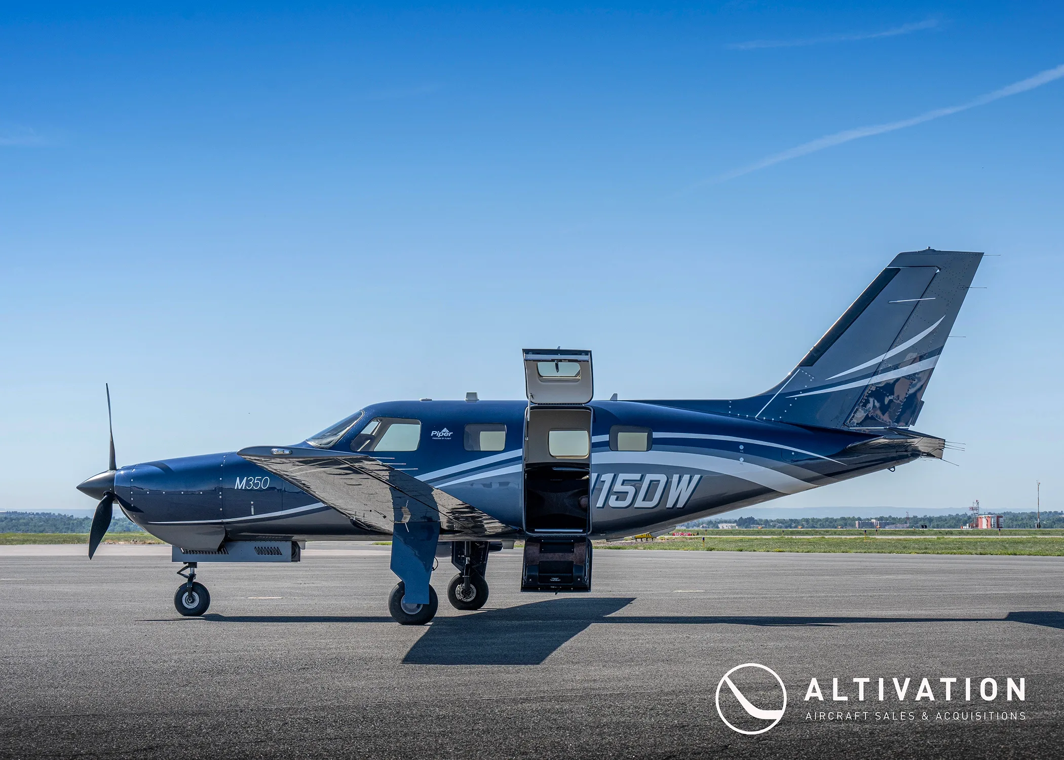 A dark blue Piper M350, tail number N115DW, parked on a tarmac with its main and cargo doors open.