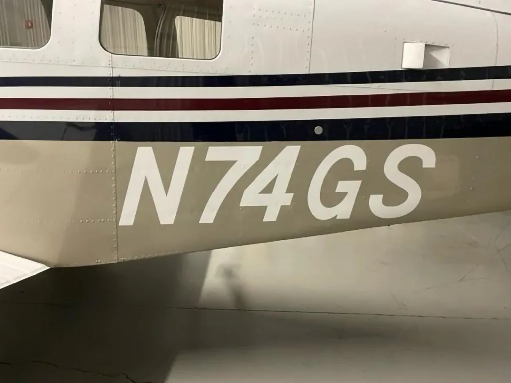 A close-up of the aircraft's fuselage showing the registration N74GS and the white, tan, dark blue, and red stripe paint scheme.