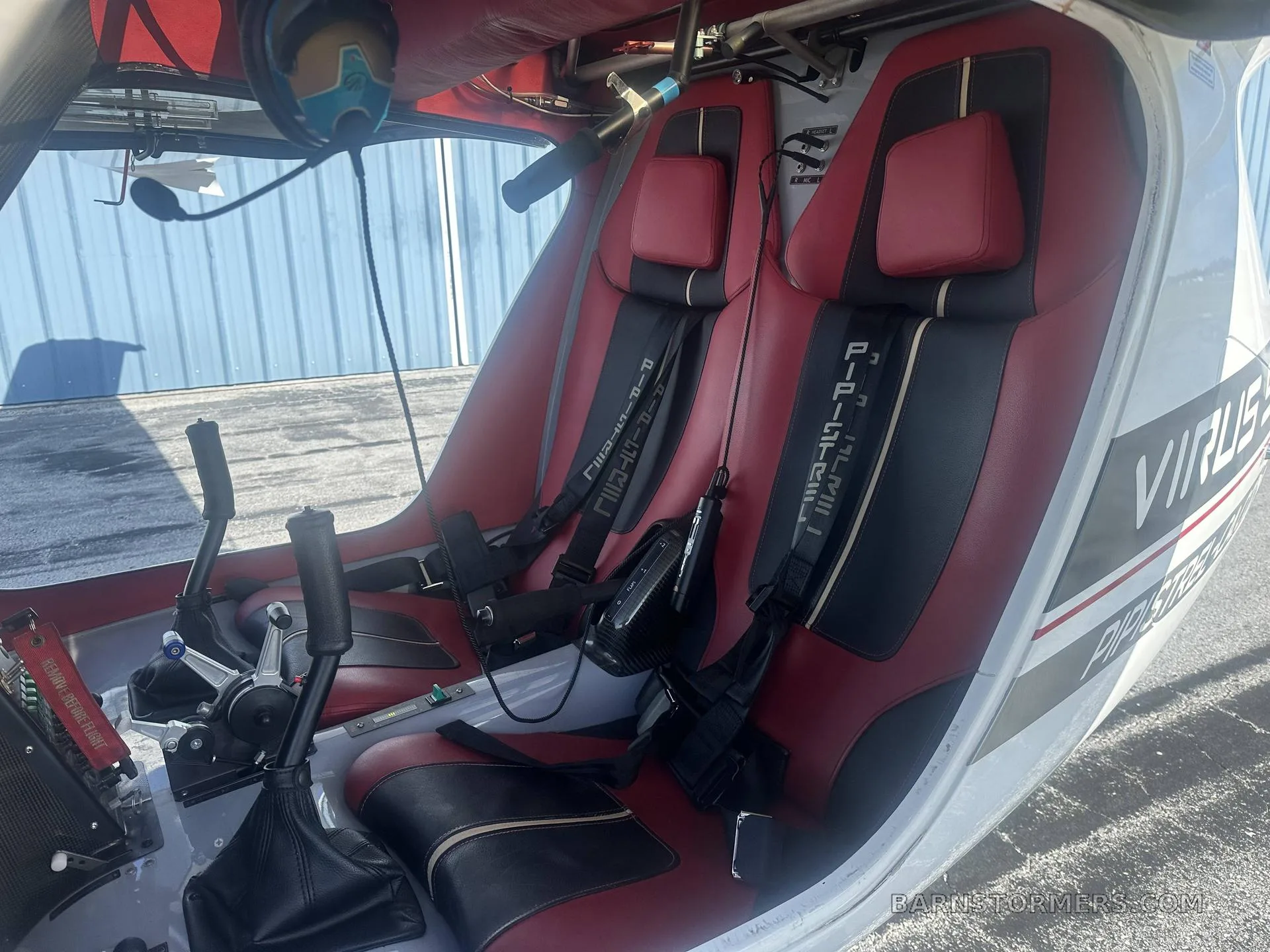 The interior of the aircraft features two red and black upholstered seats with harnesses and central control sticks.