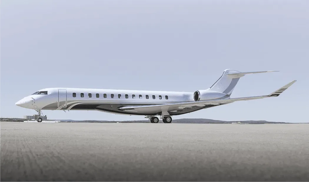 A white and grey Bombardier Global 7500 business jet parked on an airfield under a clear sky.