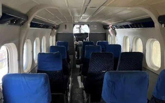 The interior cabin of an aircraft features rows of blue fabric seats and small windows along the fuselage.