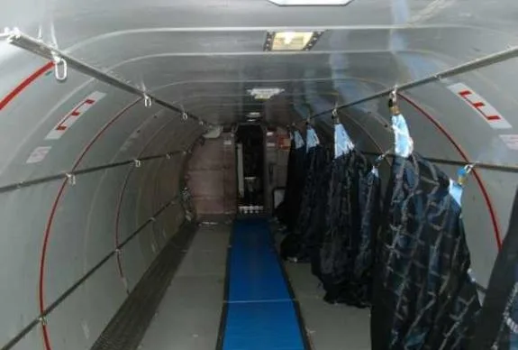 The interior of an aircraft with blue padding on the floor and black bags hanging from the ceiling.
