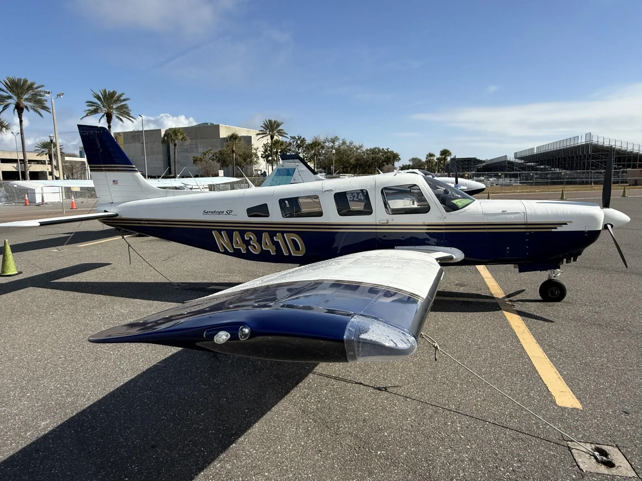 A Piper Saratoga SP (N4341D) in blue and white paint scheme parked on an airfield under a clear sky.