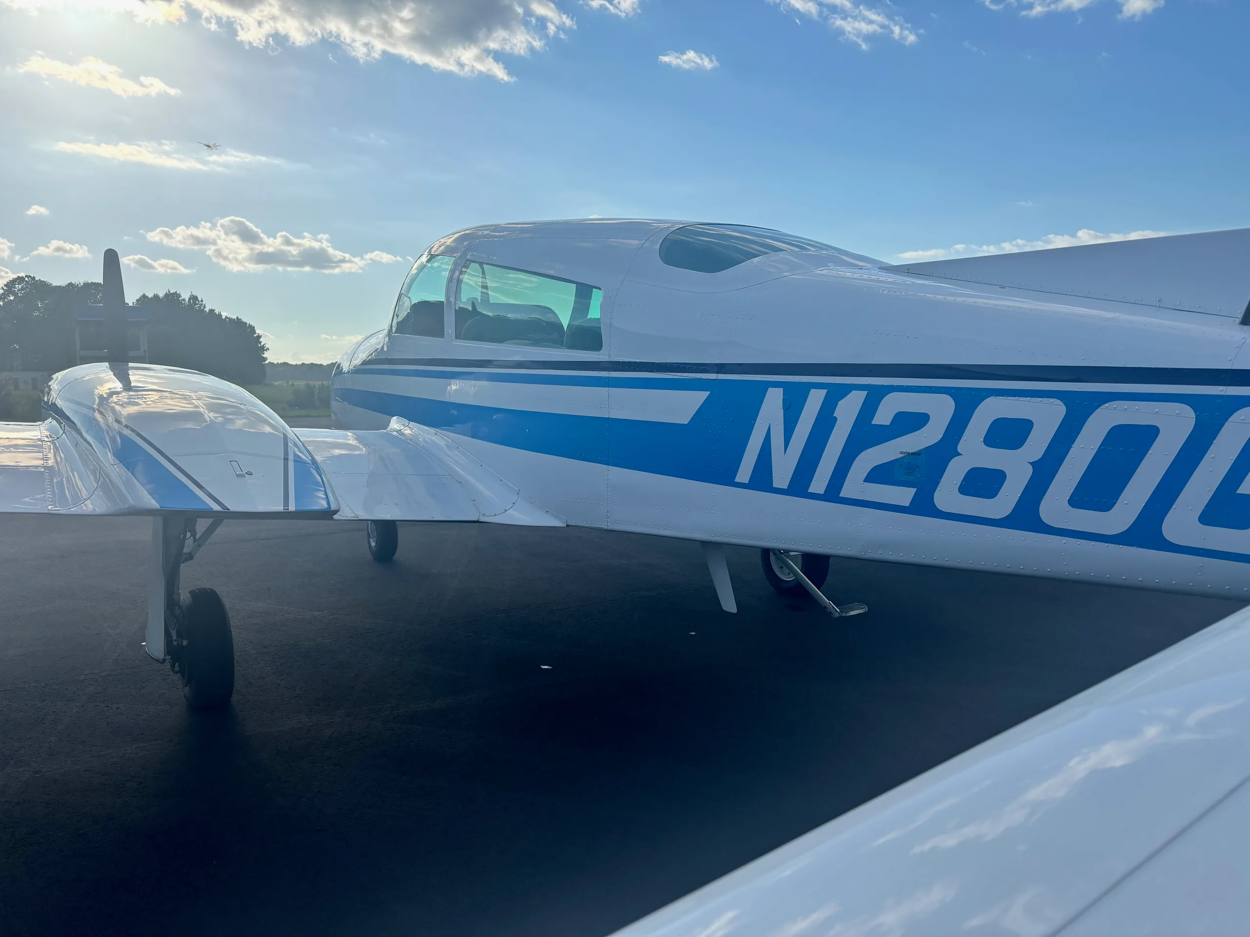 A close-up side view of the white twin-engine aircraft with blue stripes, showing the registration N1280G under a bright sky.
