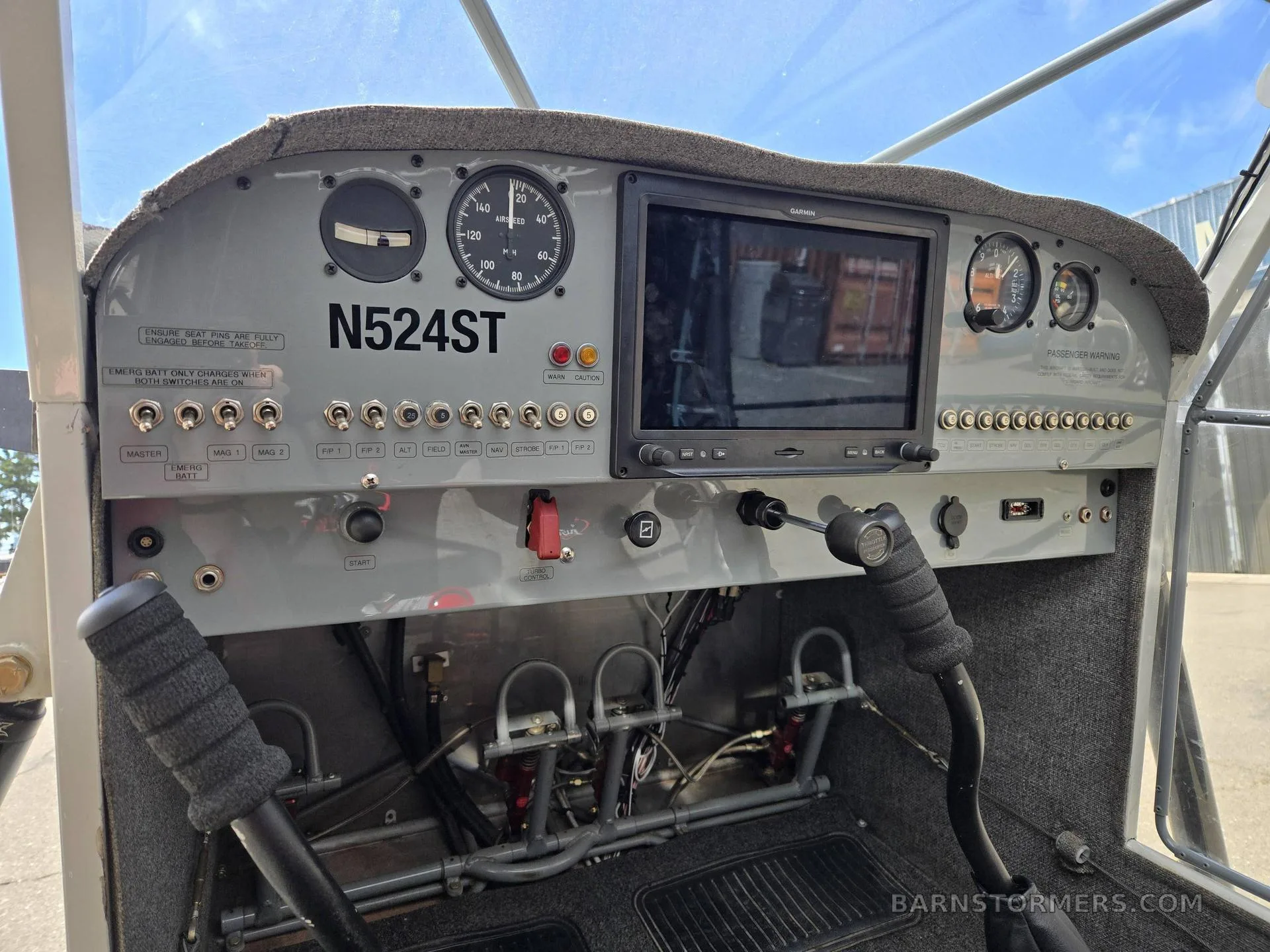 The cockpit of a light aircraft, showing the instrument panel with a Garmin display and dual control sticks.