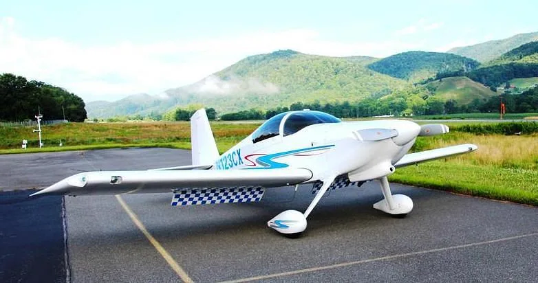 A white N123CX aircraft with blue and gray stripes parked on an asphalt runway with green mountains in the background.