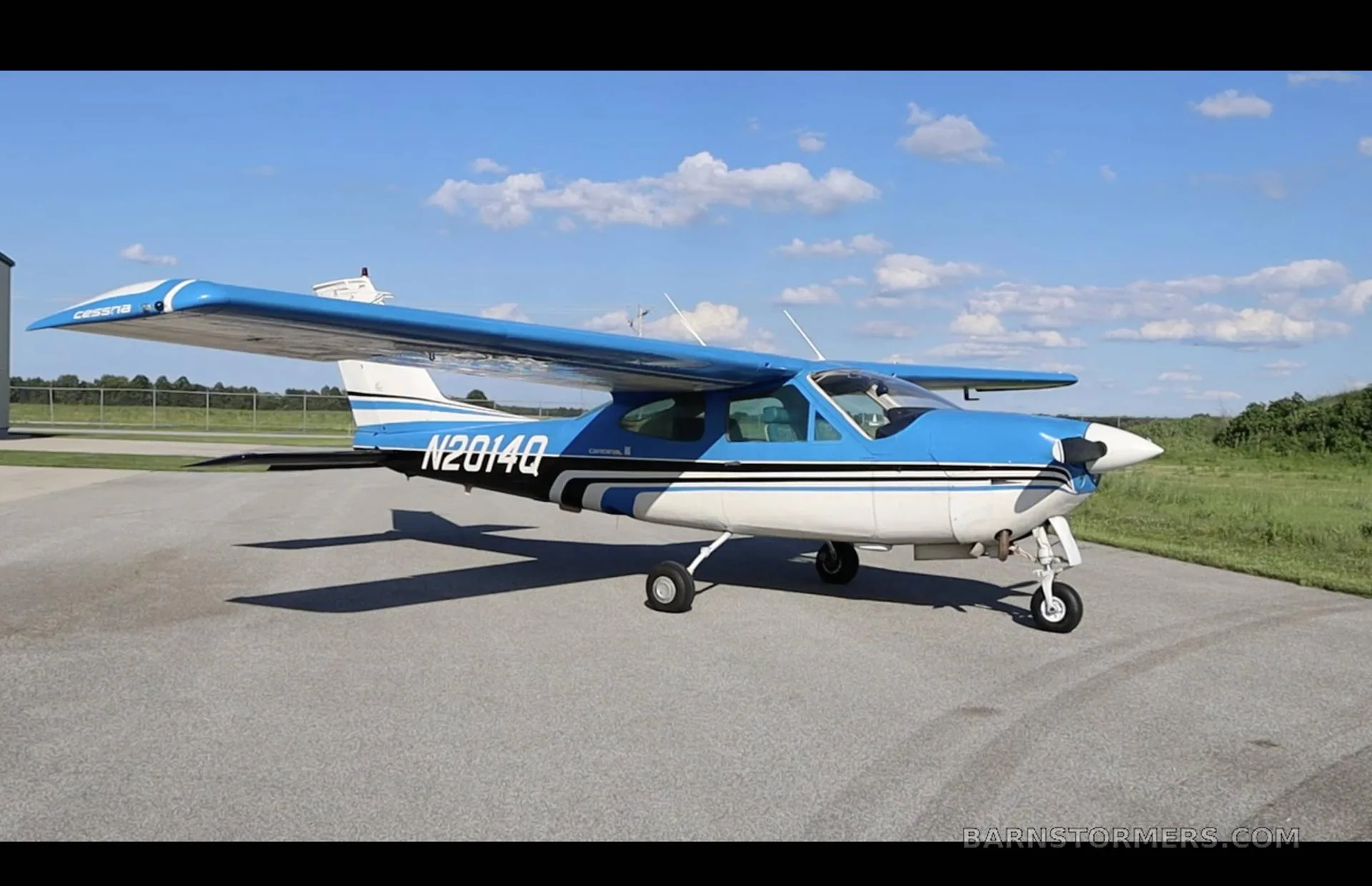 A blue and white Cessna 210 Centurion with registration N2014Q is parked on an asphalt ramp under a blue sky.