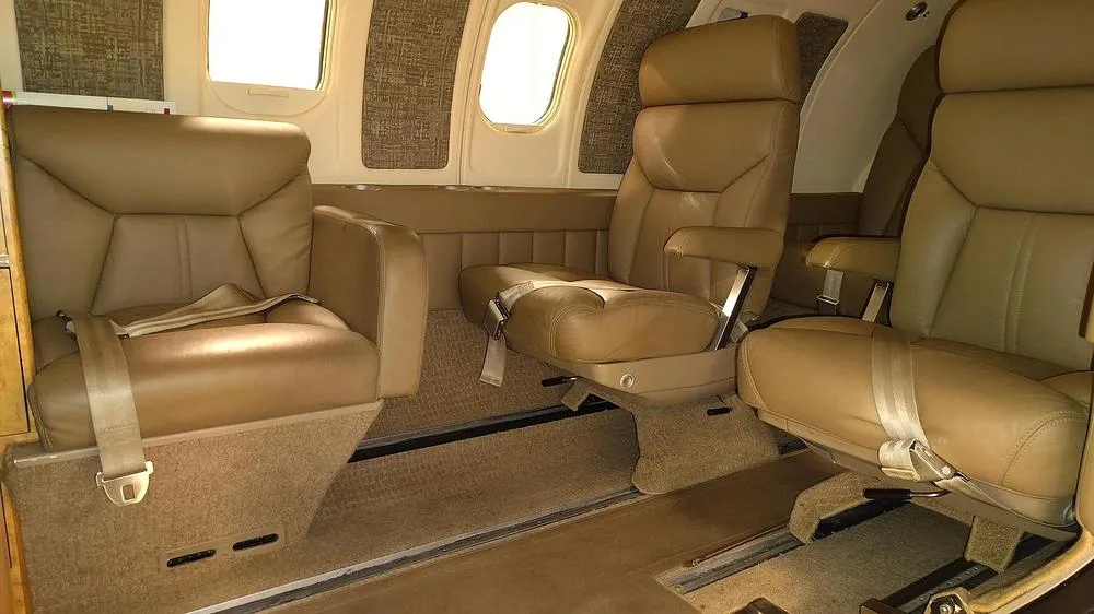 The tan leather interior cabin of a private jet, showing two forward-facing seats and one aft-facing seat.