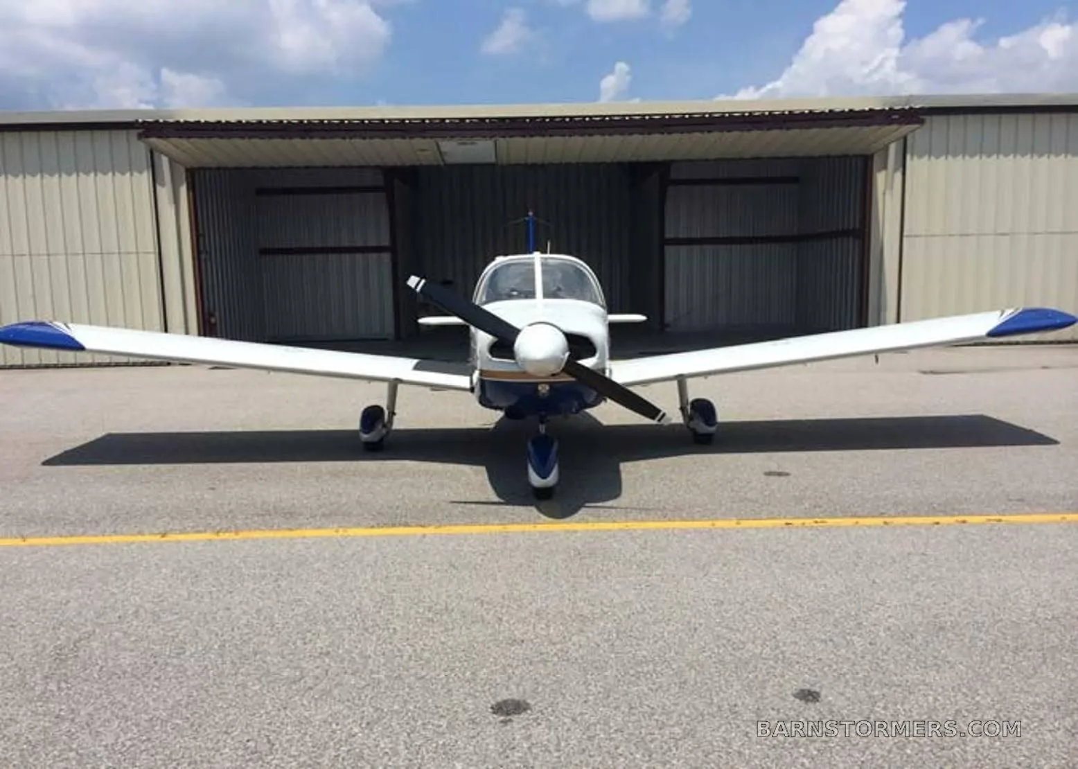 A white and blue single-engine propeller aircraft, registration N7940N, viewed from the front, parked in front of an open hangar.