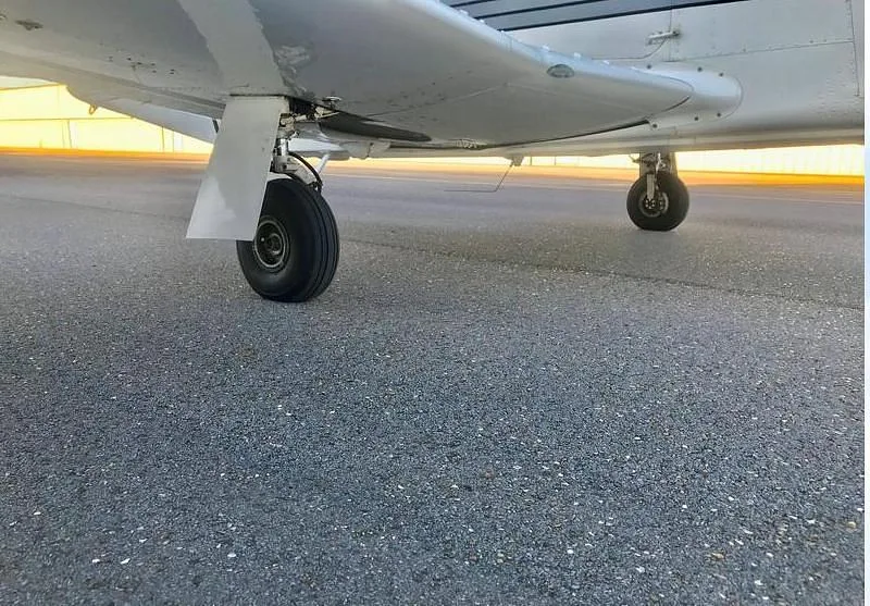 A low-angle view of the aircraft's main landing gear and the underside of its wing on an asphalt surface.