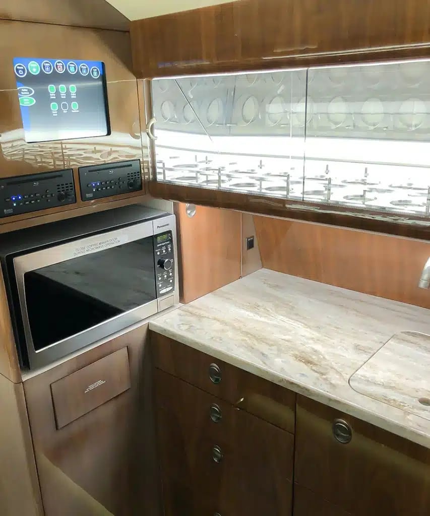 The galley area of a private jet, featuring a stainless steel microwave, a marble-patterned countertop, and a digital control panel.
