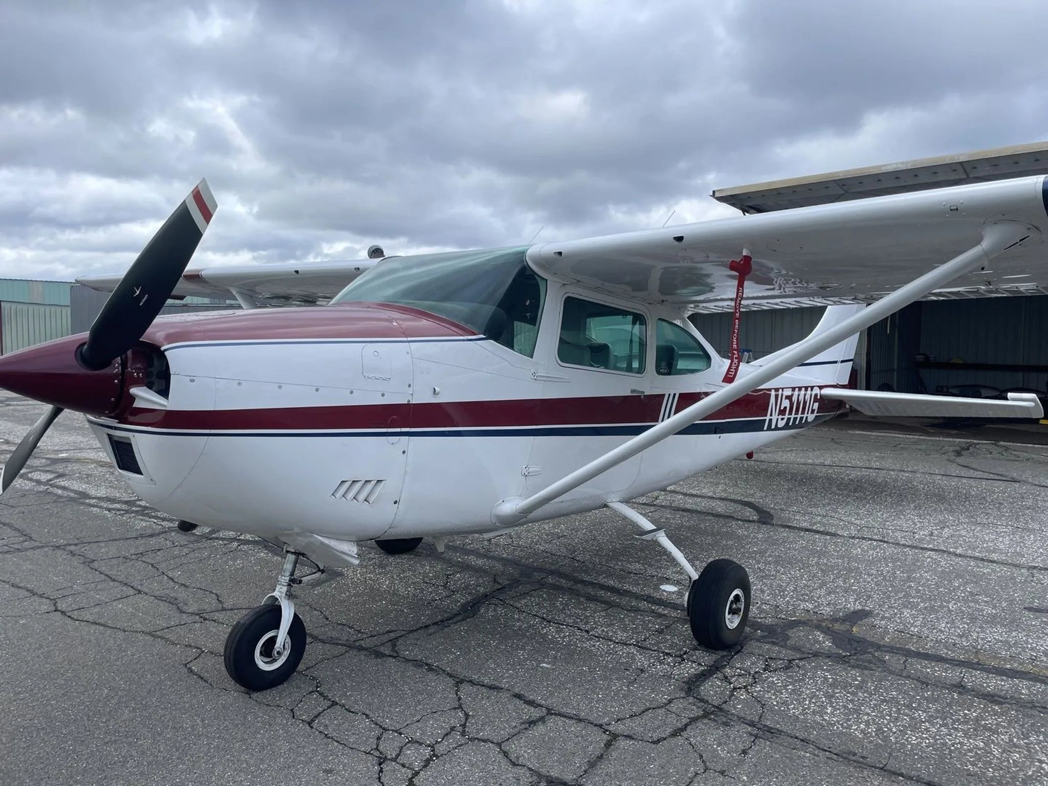 A white and maroon Cessna 182 aircraft with registration N5111G parked on a tarmac under a cloudy sky.
